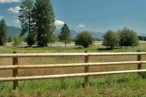A wooden fence surrounds a grassy field with mountains in the background.