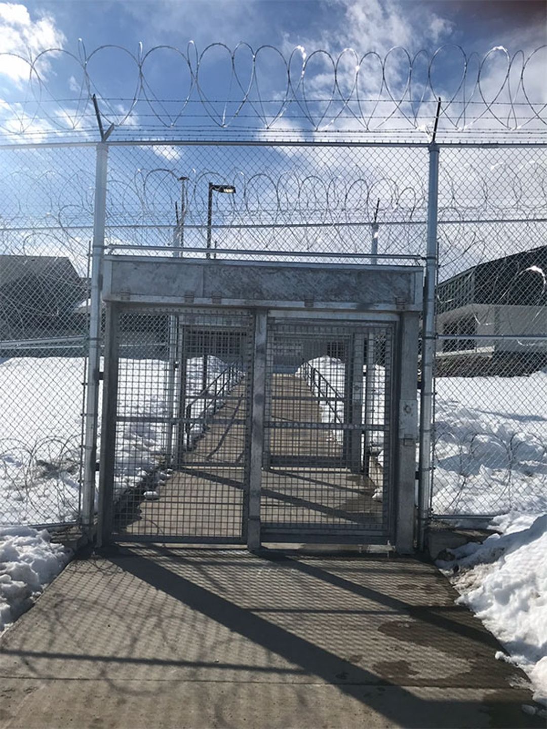 A barbed wire fence surrounds a walkway in the snow.