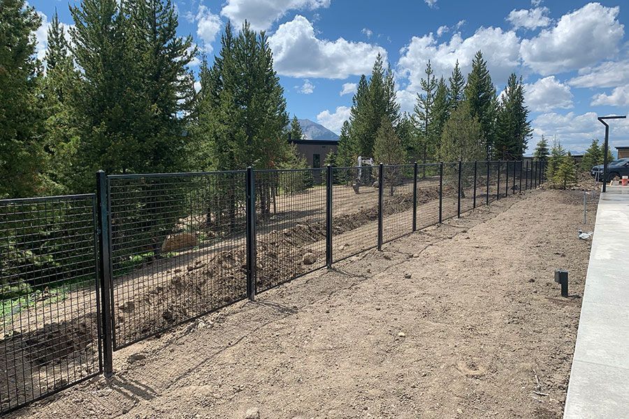 A fence is surrounding a dirt field with trees in the background.