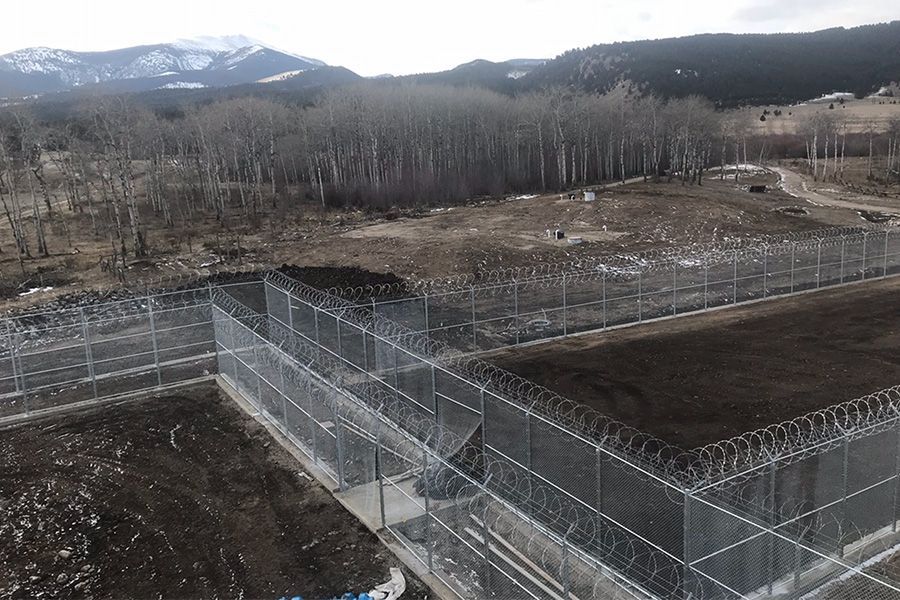 An aerial view of a prison with barbed wire fences and mountains in the background.