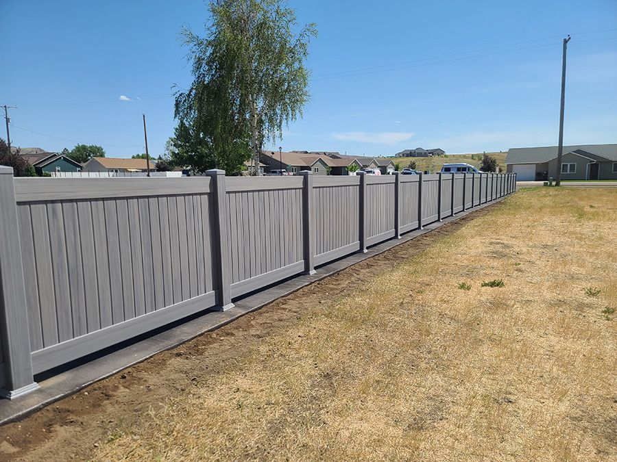 A gray fence surrounds a grassy field in a residential area.