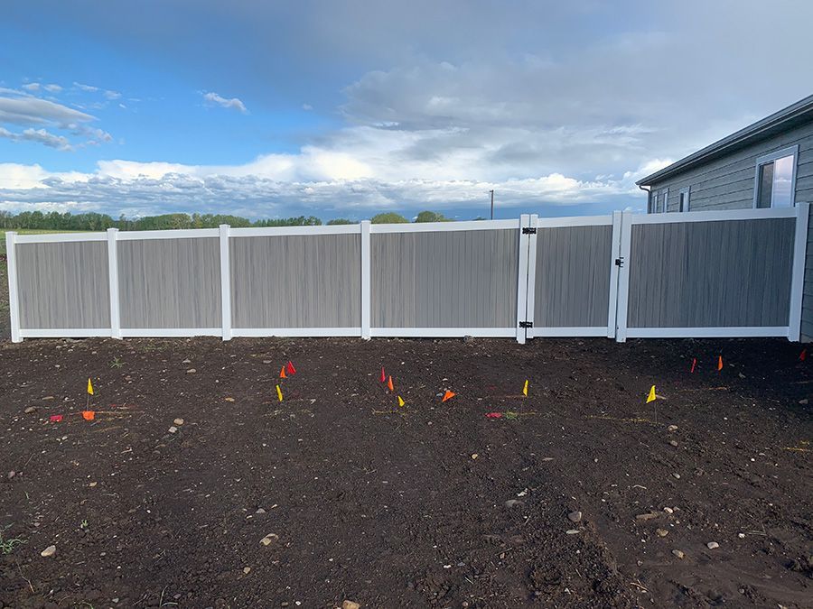 A gray and white fence with a gate is in the middle of a dirt field.