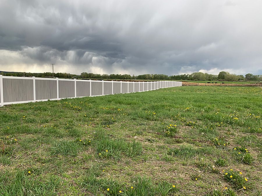 A long white fence surrounds a grassy field with a cloudy sky in the background.