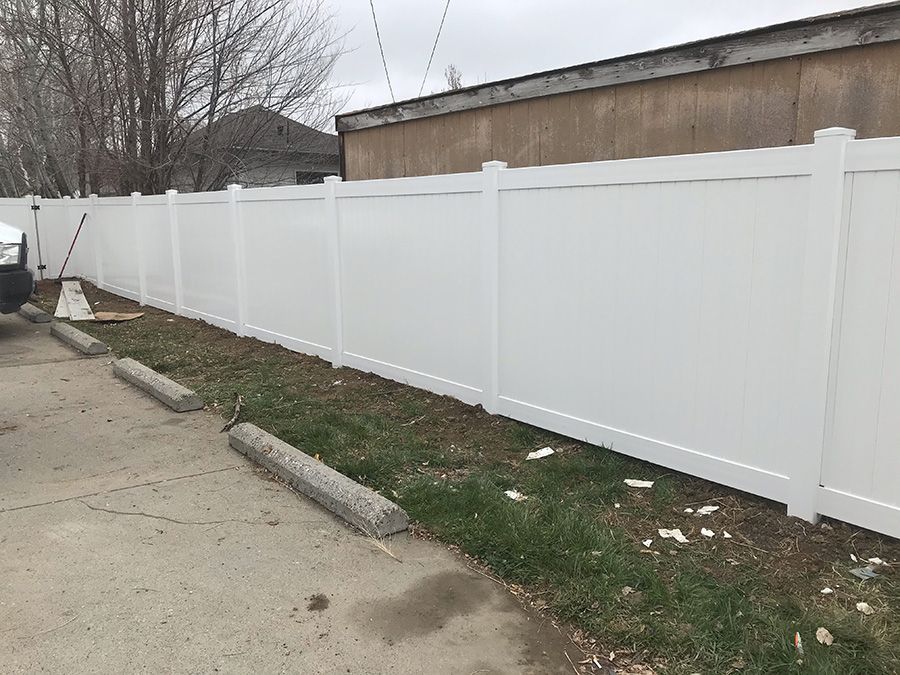A white vinyl fence is sitting next to a parking lot.