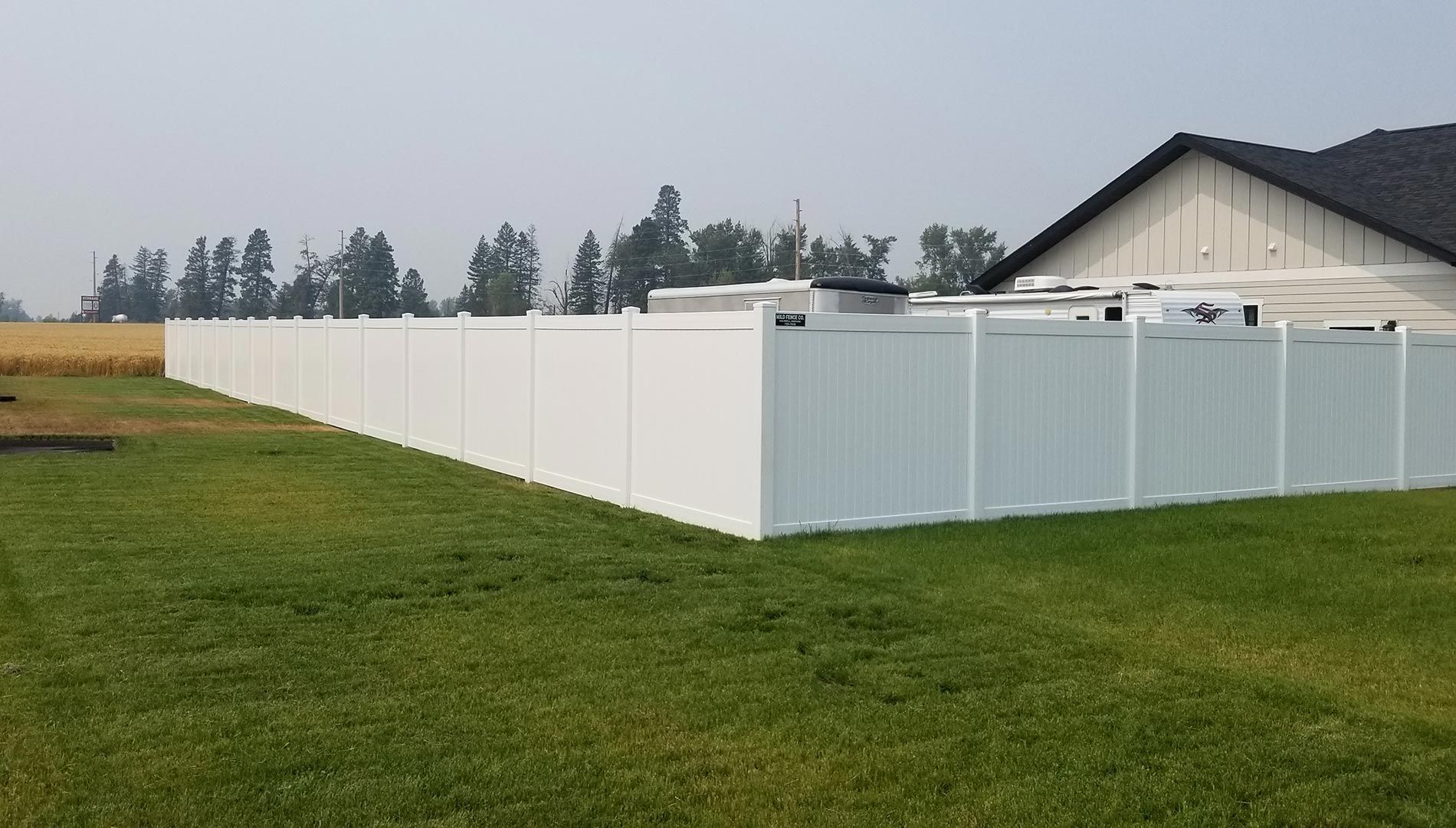 A white fence surrounds a lush green field in front of a house.