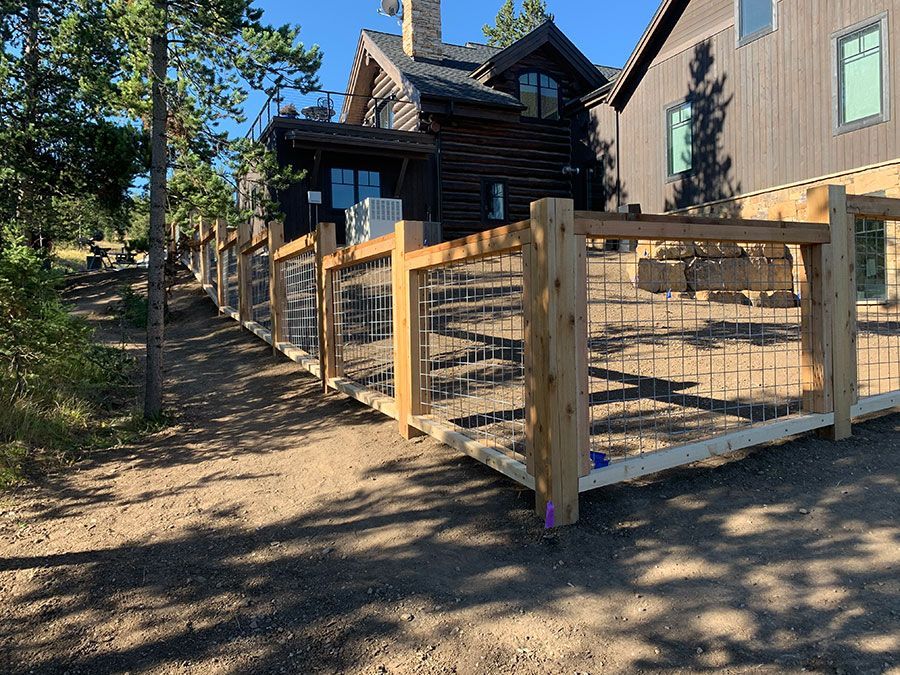 A wooden fence is surrounding a dirt road in front of a house.