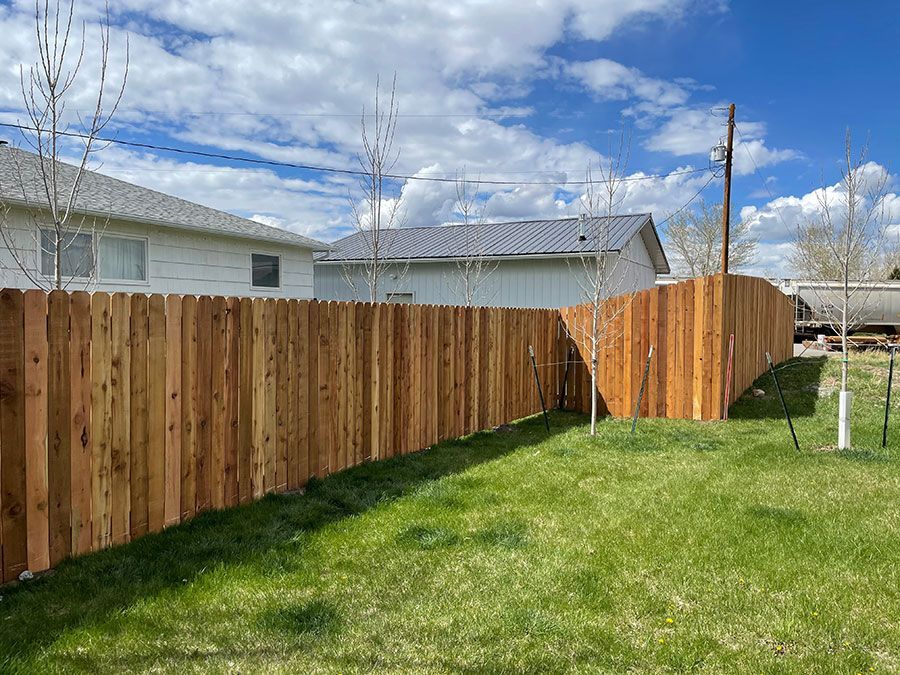 A wooden fence surrounds a lush green yard in front of a house.