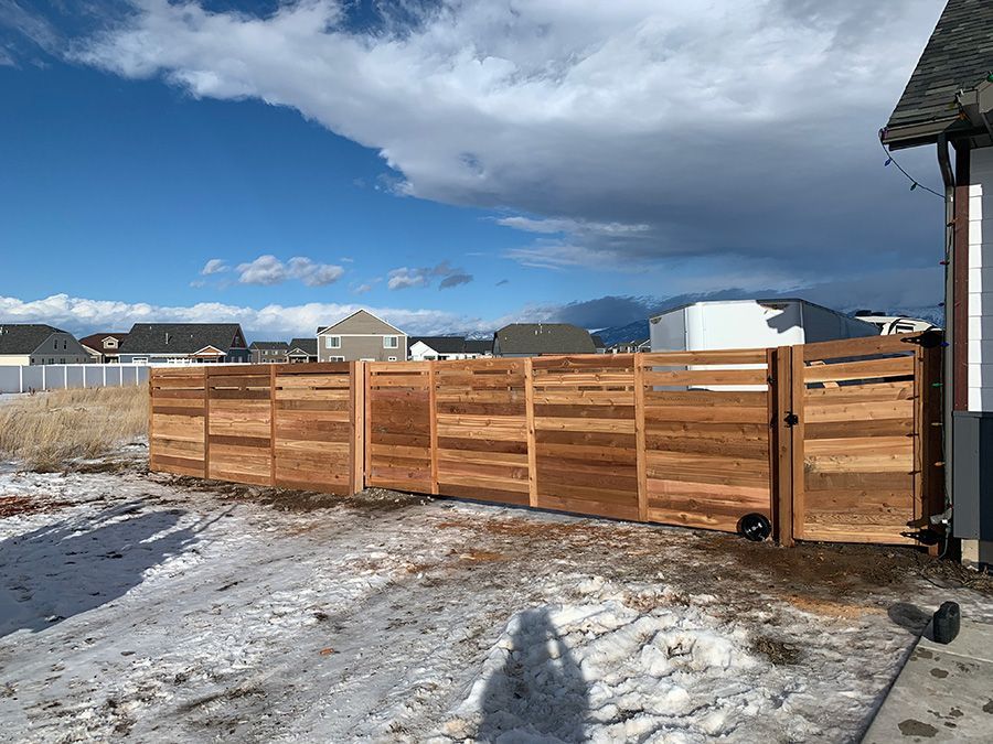A wooden fence is sitting in the snow in front of a house.
