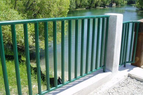 A green railing overlooking a lake with trees in the background