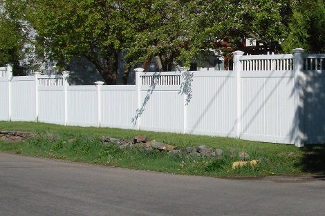 A white fence surrounds a grassy area next to a road