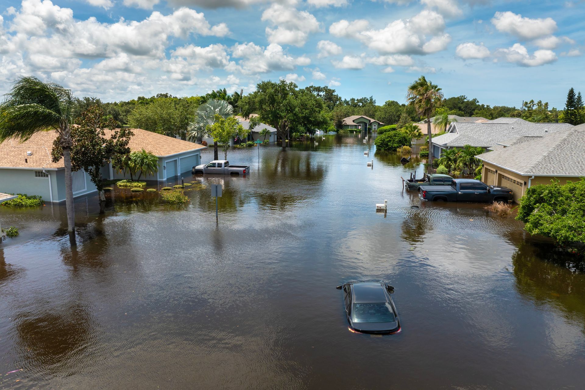 Flooded residential street with submerged cars and homes under a cloudy sky
