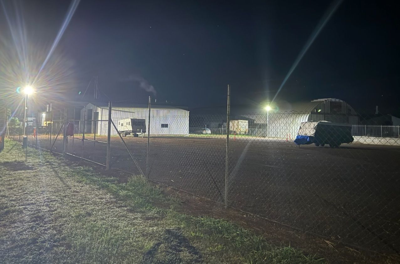 A dirt lot at night illuminated by two bright streetlights, with a white building and a dark vehicle in the background Tableland Self Storage In Atherton, QLD