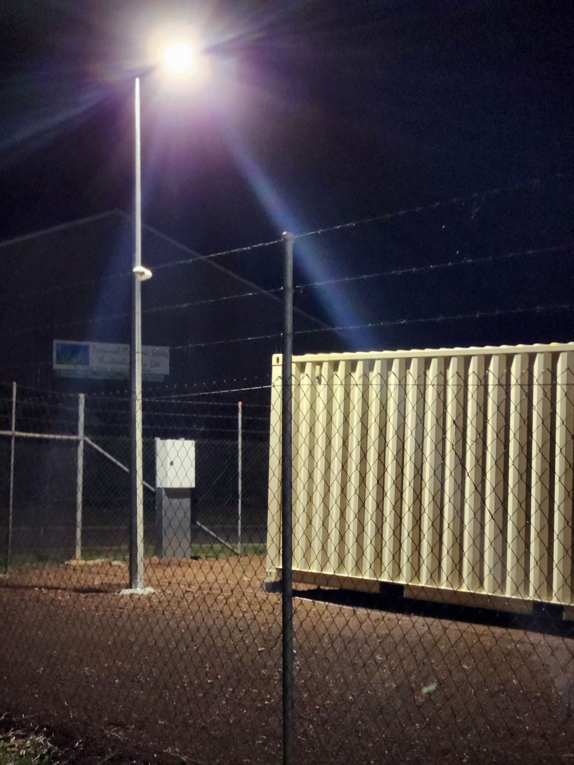 A bright streetlamp illuminates a fenced area at night, highlighting a shipping container and an electrical box Tableland Self Storage In Atherton, QLD