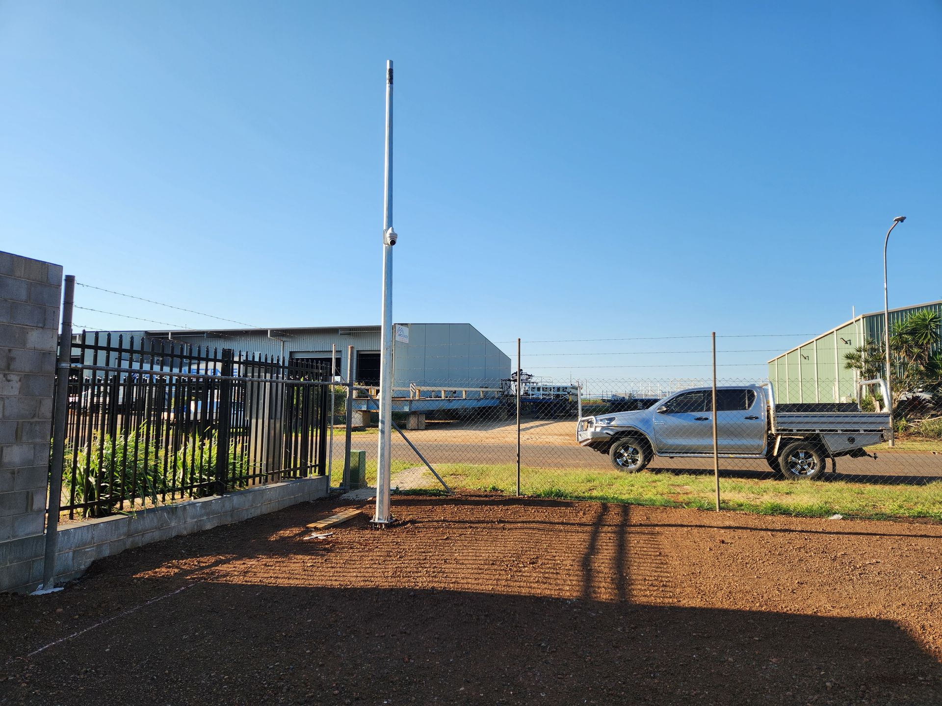 A tall, white pole stands in a fenced-in dirt yard, with a silver pickup truck parked behind a gate in the background Tableland Self Storage In Atherton, QLD