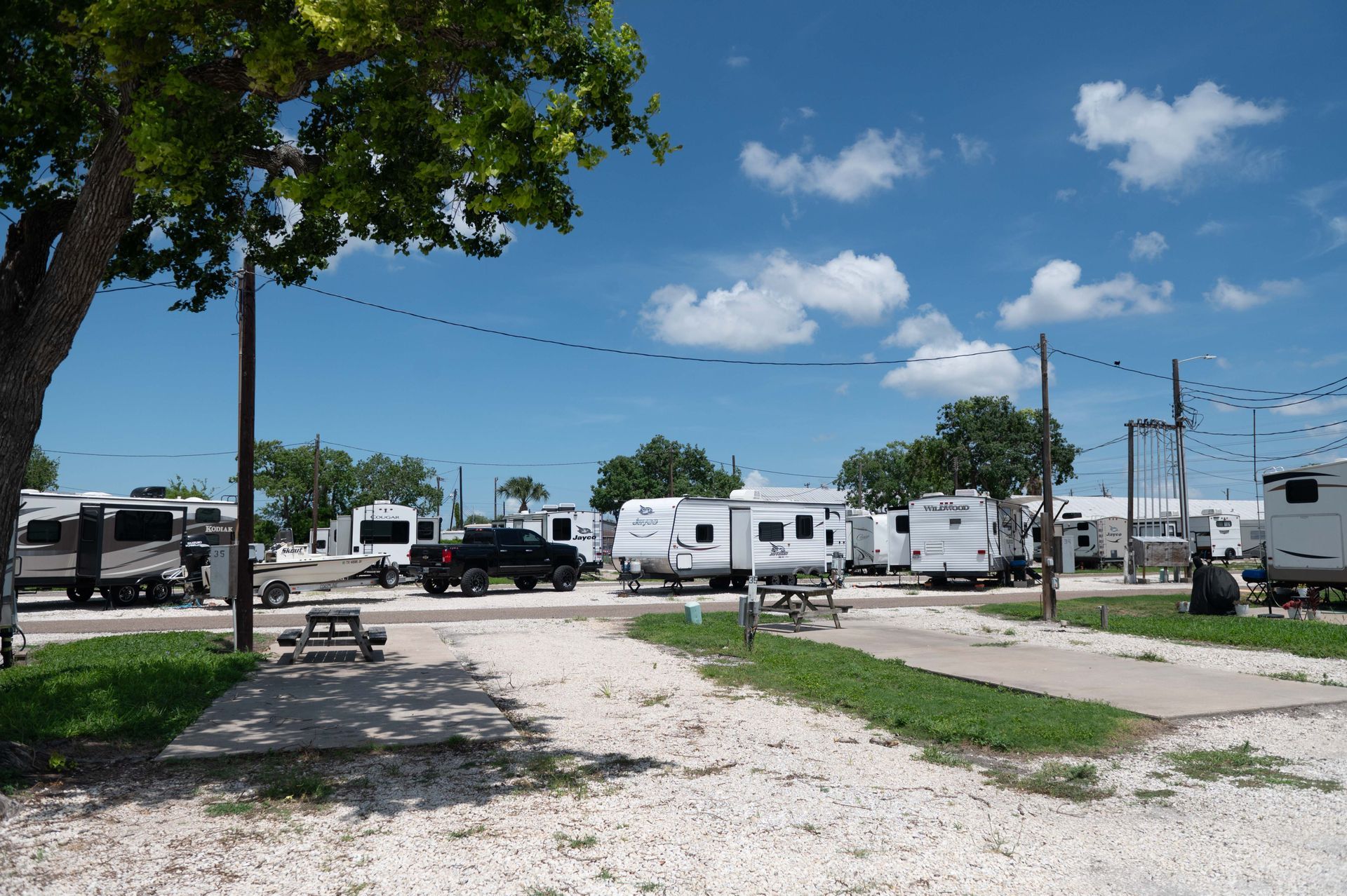 RV park with parked campers and trailers under a bright blue sky, viewed from a gravel lot