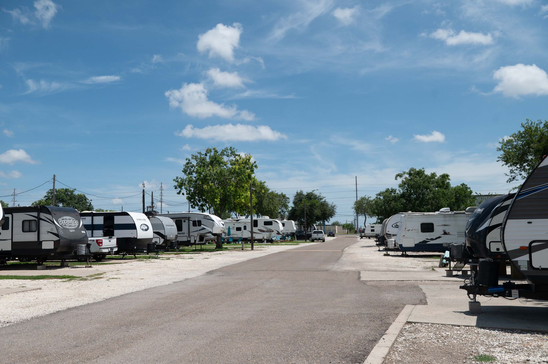 RV campground with parked trailers along a gravel road under a blue sky and scattered clouds
