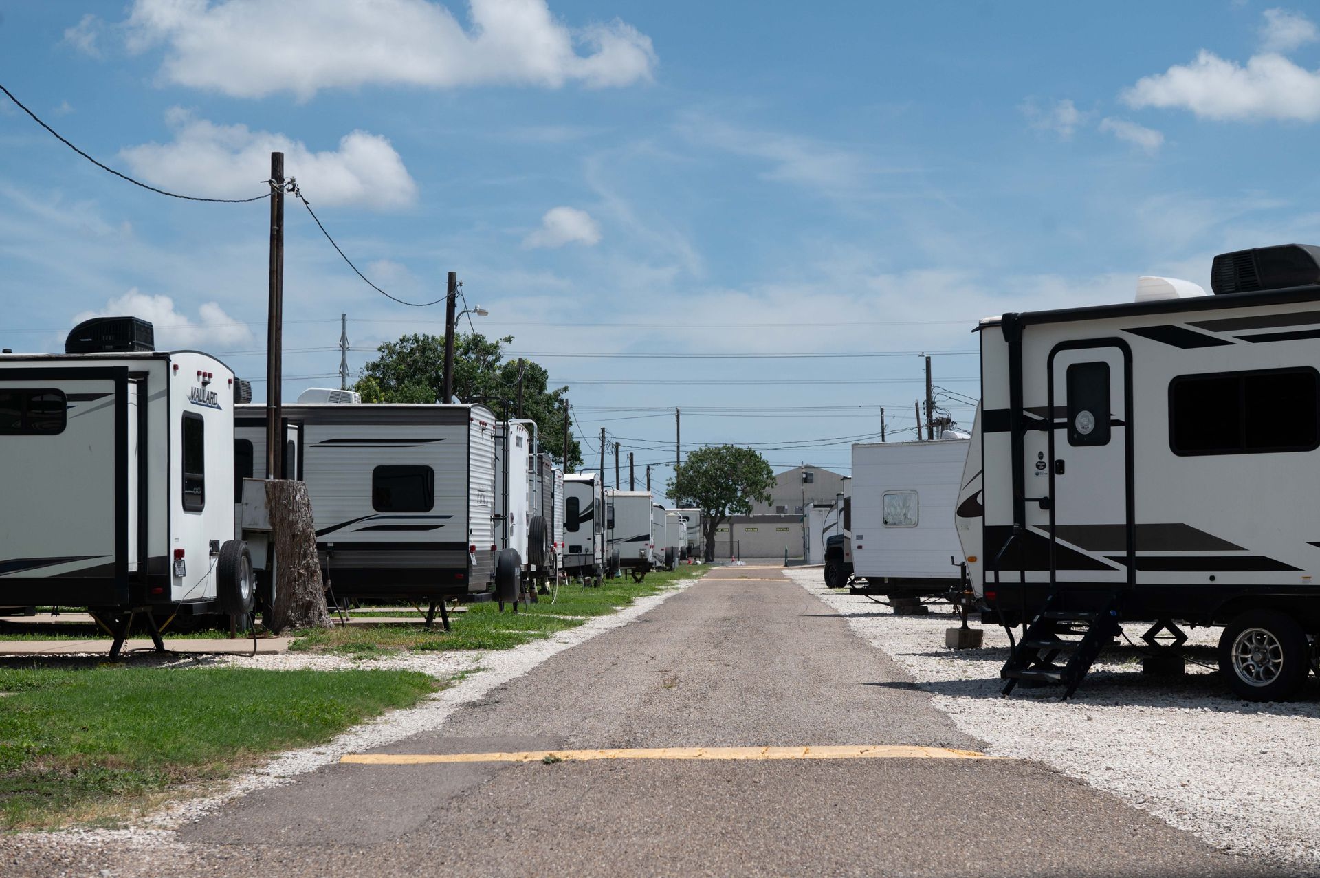 Rows of white RV trailers lining a gravel road under a blue sky with utility poles