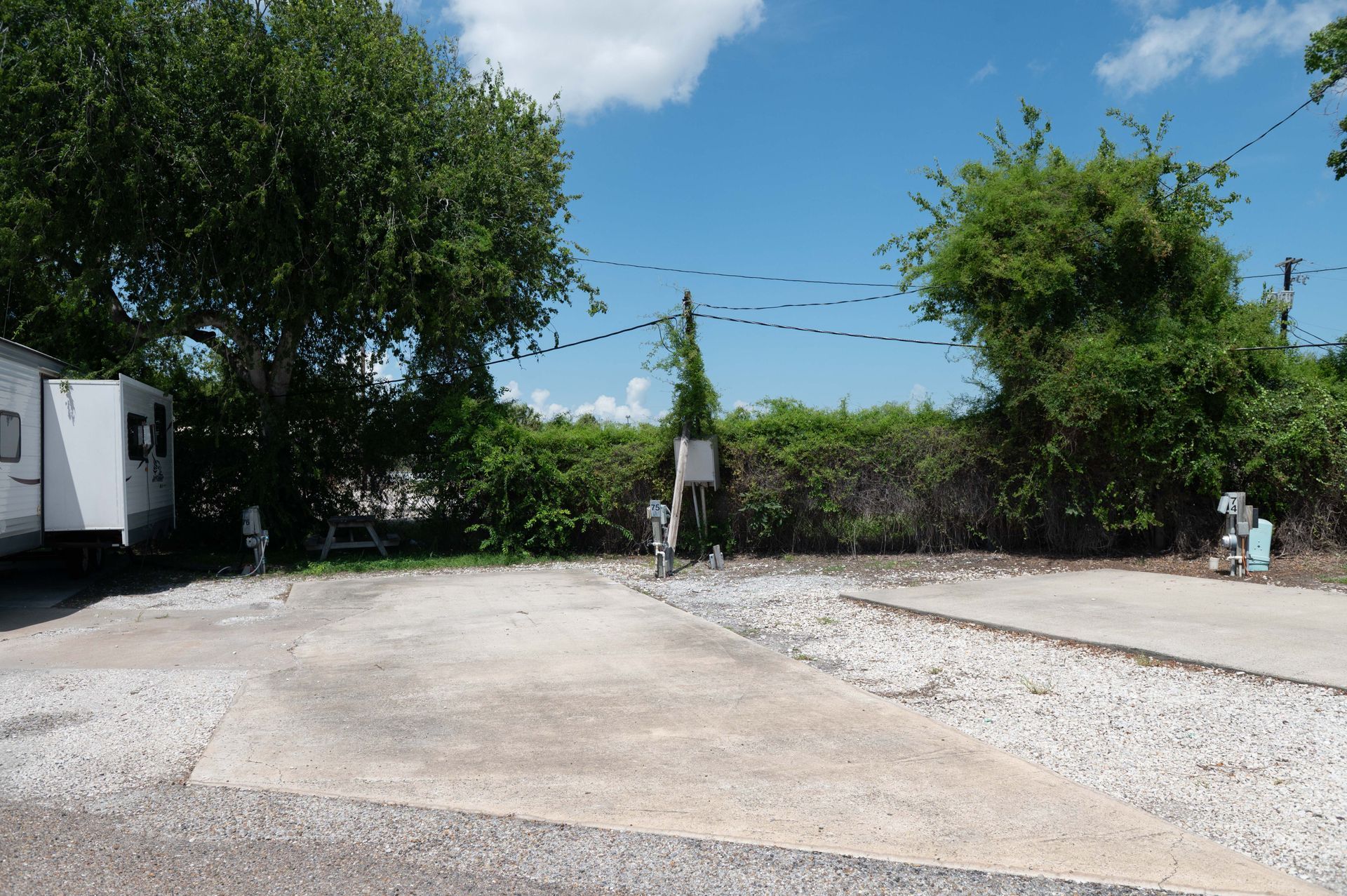 Open gravel driveway with trees, blue sky, and a small white trailer on the left