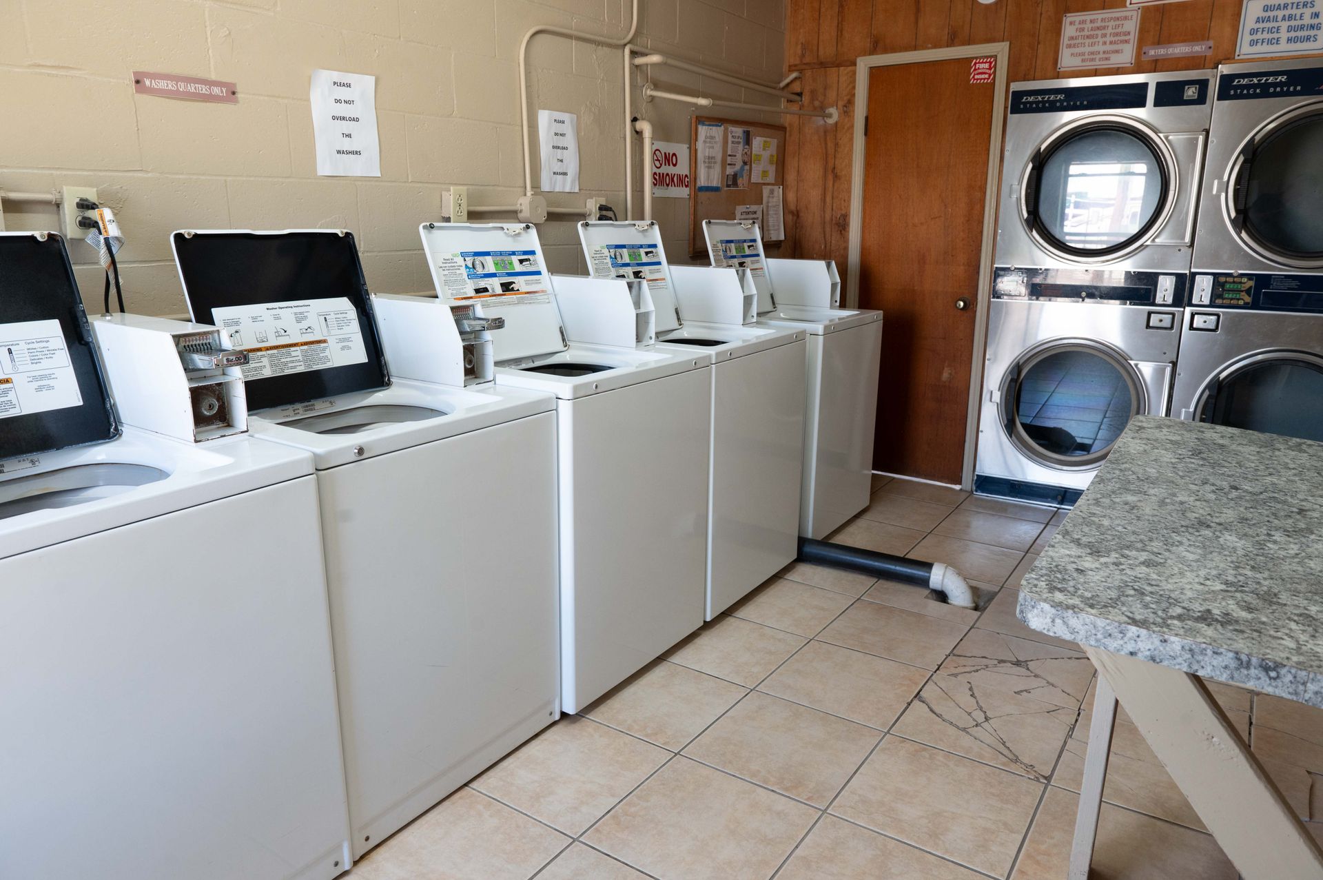 Laundry room with rows of white washers and dryers, folding table, and tiled floor