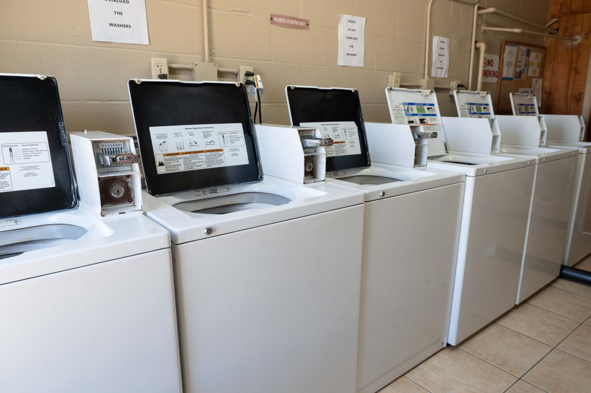 Row of white washing machines with open lids and control panels in a laundromat showroom