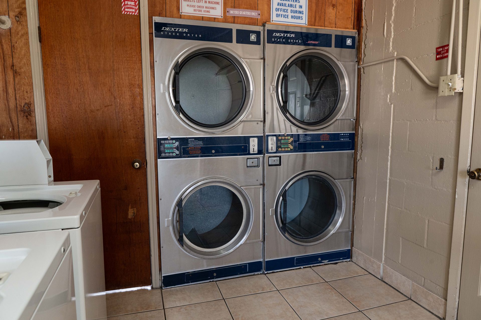 Stacked front-load laundromat dryers and washers in a tiled laundry room.