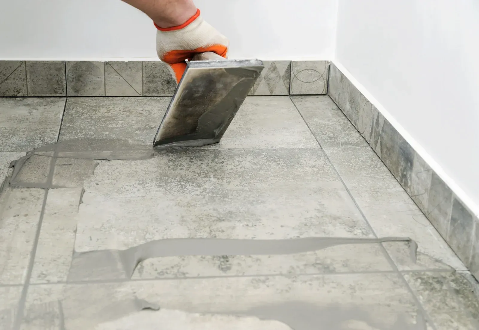 A person is applying grout to a tiled floor with a trowel.