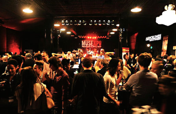 A crowded venue with people facing a stage lit up with the words