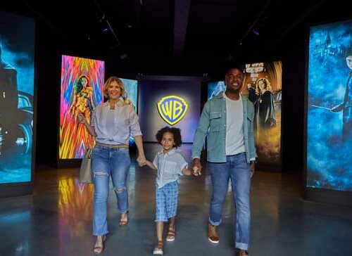 Family of three walking toward a Warner Bros. logo, surrounded by colorful movie posters.