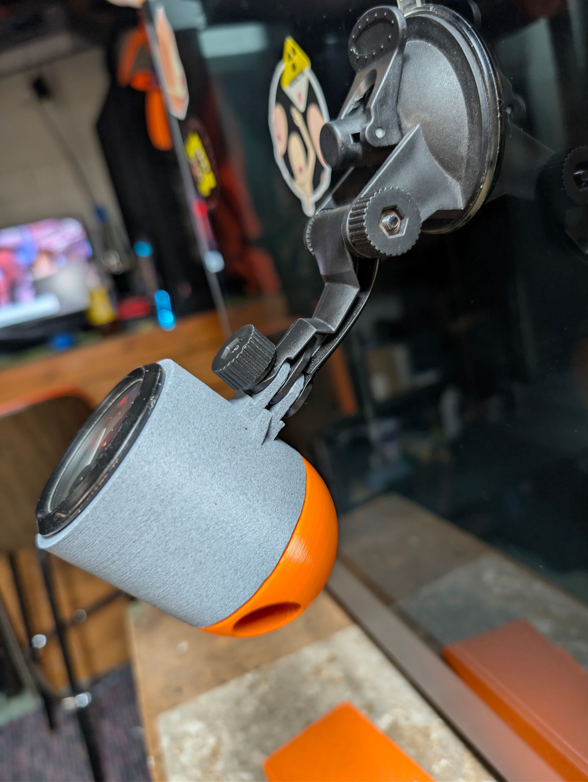 Gray and orange 3D-printed part clamped in a black mount, hanging over a workbench