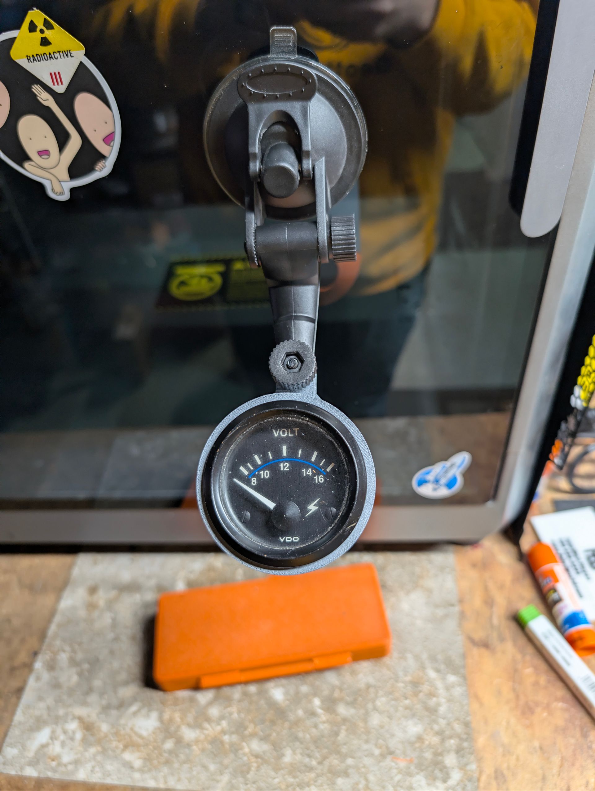 Gray and orange 3D-printed part clamped in a black mount, hanging over a workbench