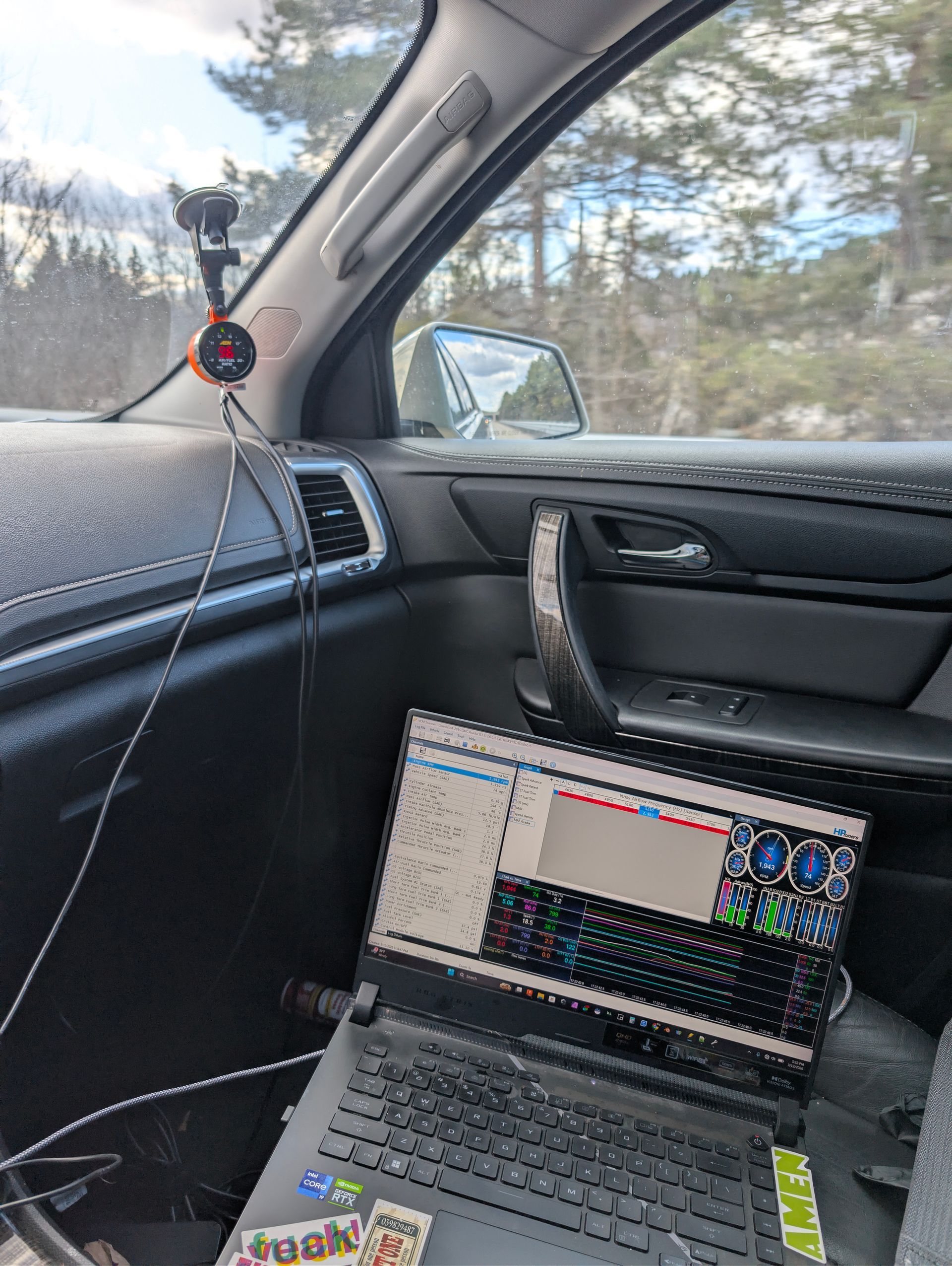 Laptop open on a car passenger seat, showing a screen with tuning software, near a window and dashboard gauge pod