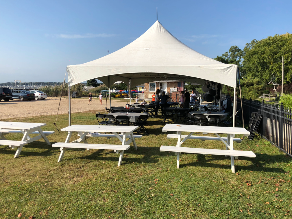 A group of white picnic tables under a white high-peak tent.