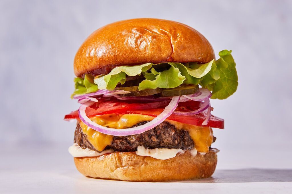 A hamburger with cheese , lettuce , tomato , onions and pickles on a bun.