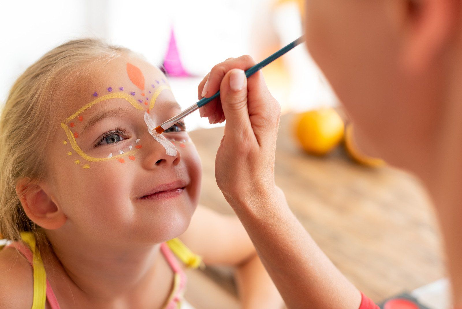A little girl is getting her face painted by a woman.