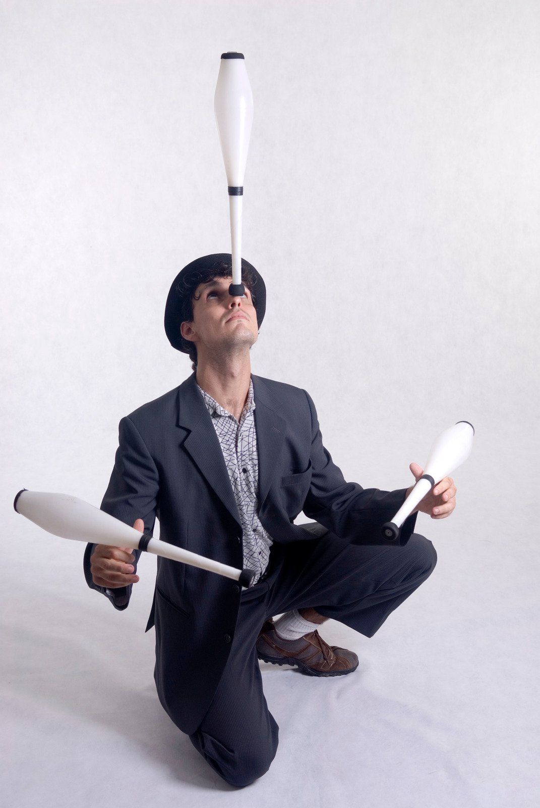 A man in a suit is juggling two clubs on his head