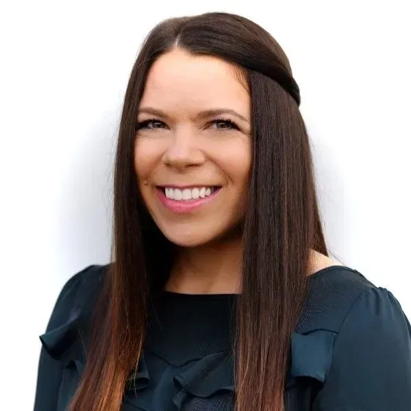 Woman with long dark hair smiles, wearing a dark top, against a white background.
