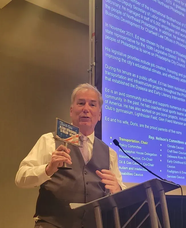 Man speaking at a podium, holding an award. Presentation screen in the background.