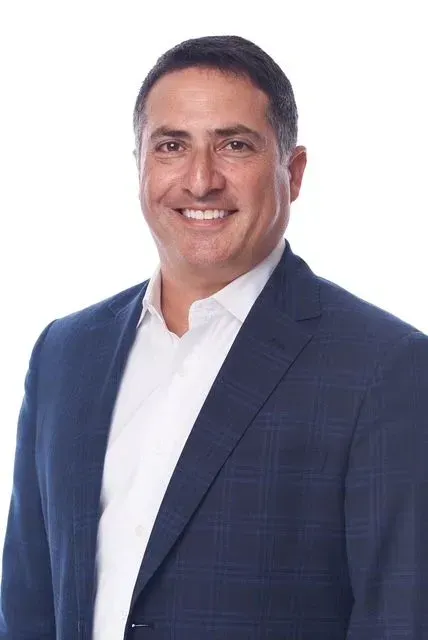 Man in a navy blazer and white shirt smiles, against a white background.