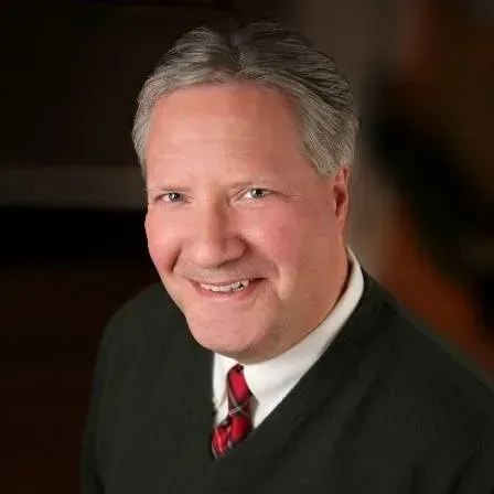 Man in a sweater and tie smiles at the camera, headshot.