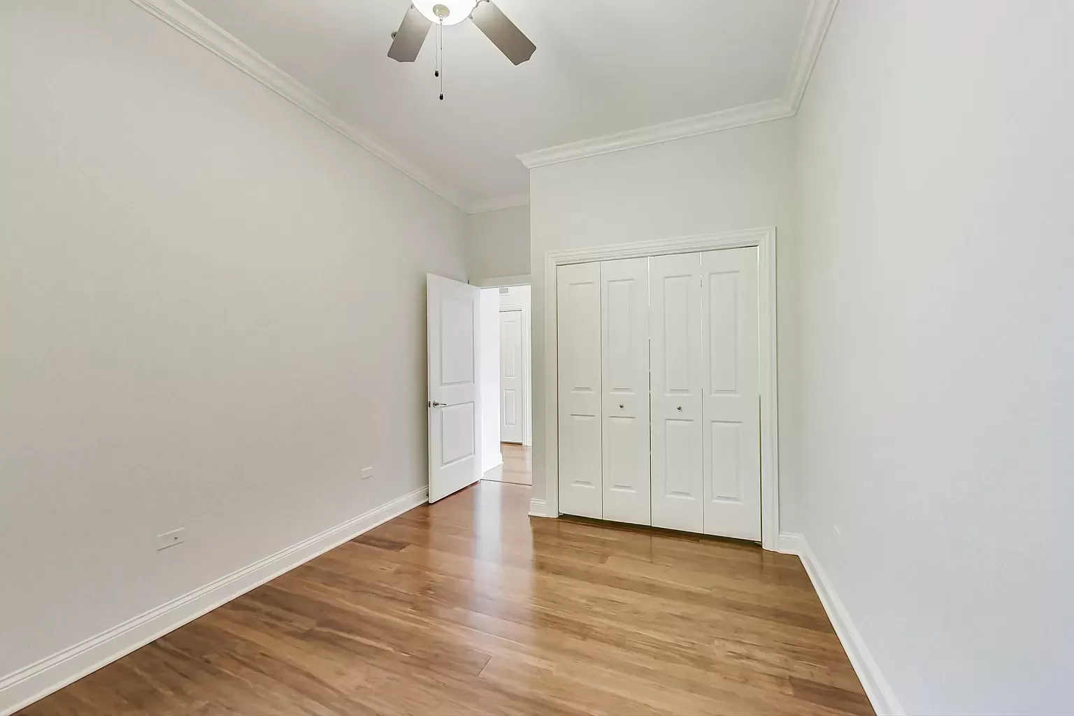 an empty bedroom with hardwood floors and a ceiling fan .