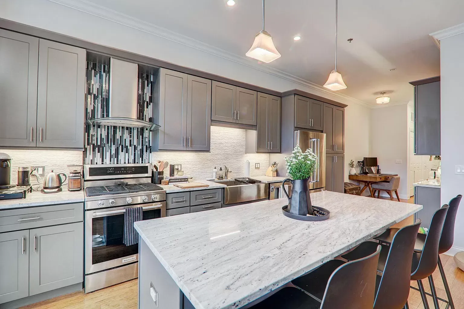 a kitchen with gray cabinets , stainless steel appliances , granite counter tops and a large island .