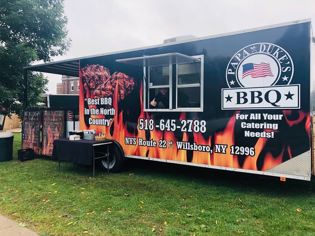 A bbq food truck is parked in a grassy field.