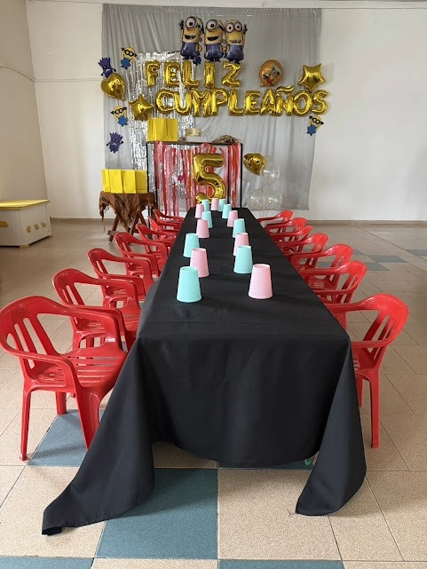 Mesa de fiesta decorada con un mantel negro, sillas rojas y vasos en tonos pastel en una habitación temática de los Minions