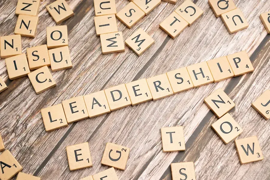 Scrabble tiles spelling “LEADERSHIP” on a wooden surface, with scattered letter tiles around it