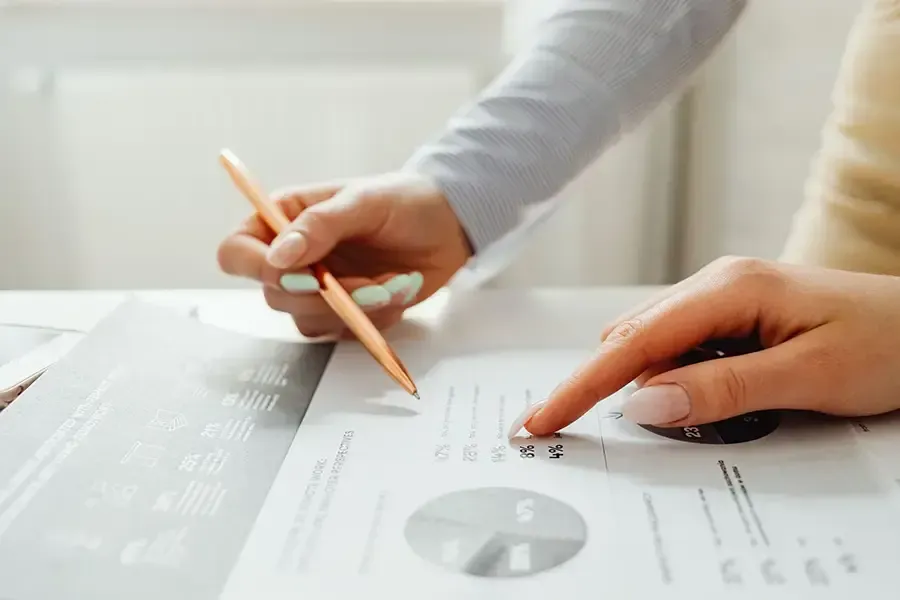 Hands pointing at financial charts and graphs on a desk with a pencil