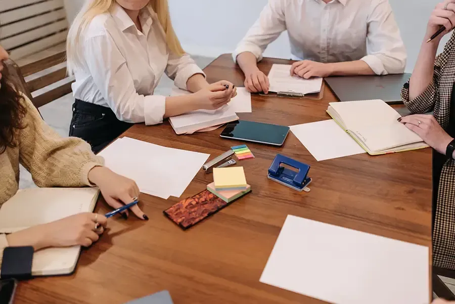 People around a wooden table reviewing papers, notebooks, and smartphones in a meeting.
