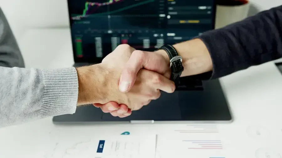 Business handshake over a laptop with charts on screen