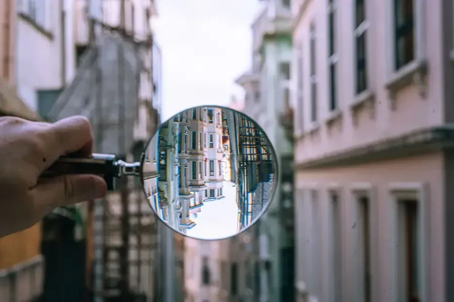 Hand holding a magnifying glass reflecting a narrow street between buildings