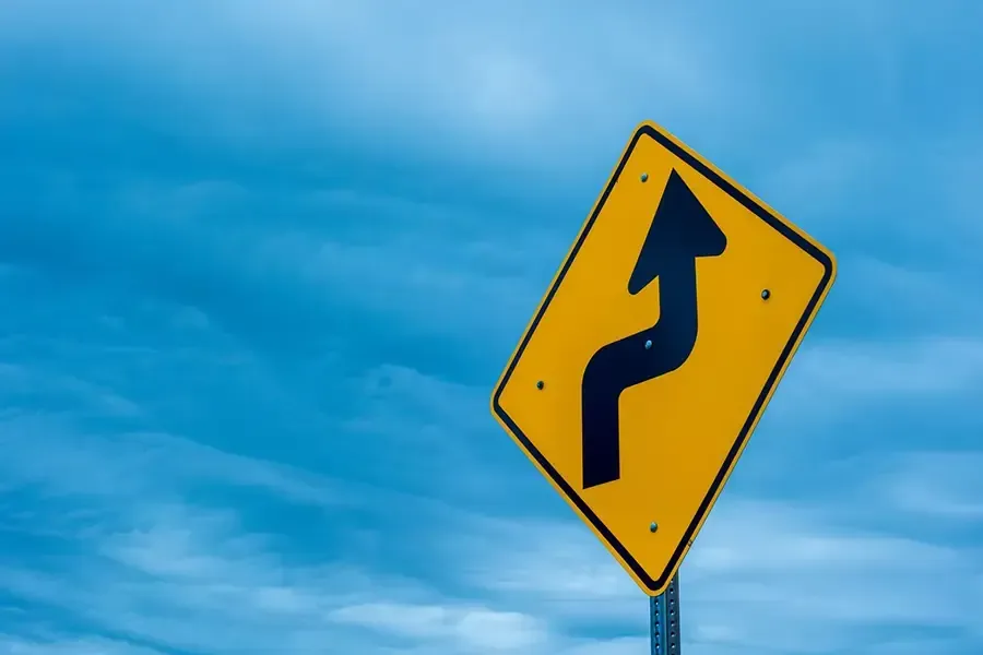 Yellow winding road sign against a blue sky