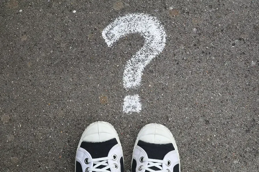 White question mark on pavement above black-and-white sneakers pointing toward it